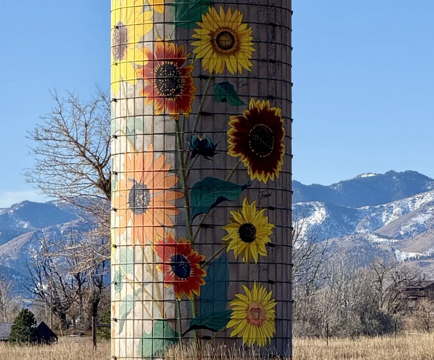 Painted sunflower post beside a gravel road with mountain views